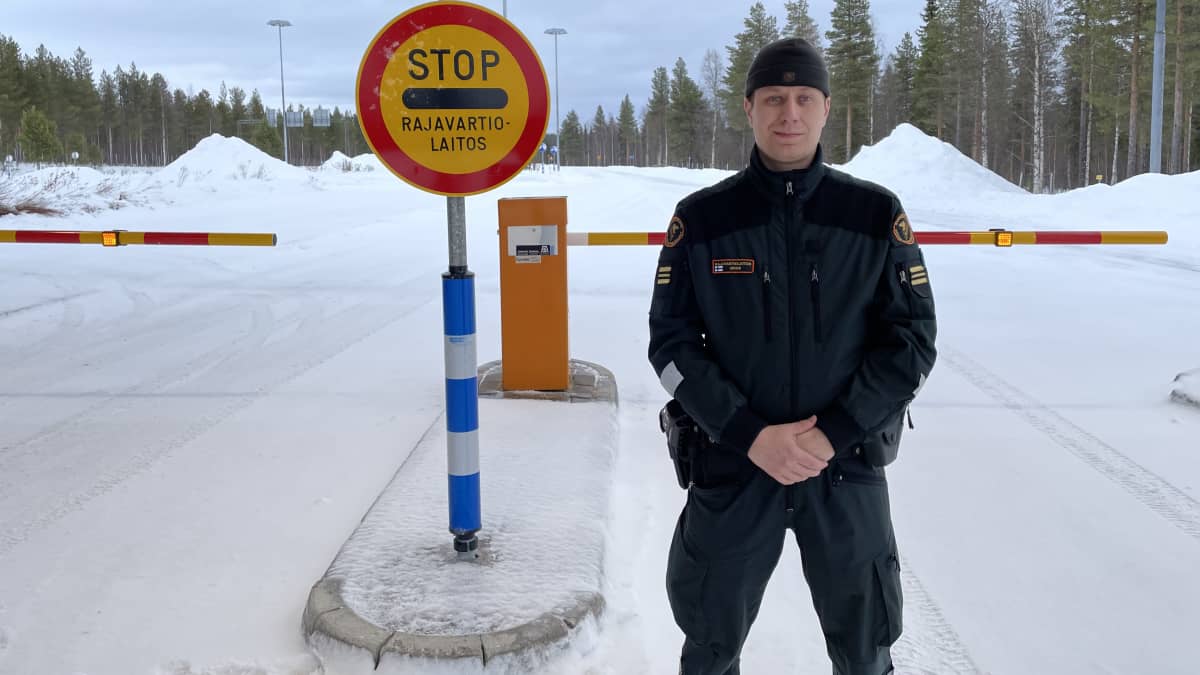 Rajavartija seisoo talvisessa maisemassa rajavartiolaitoksen ajopuomin edessä.