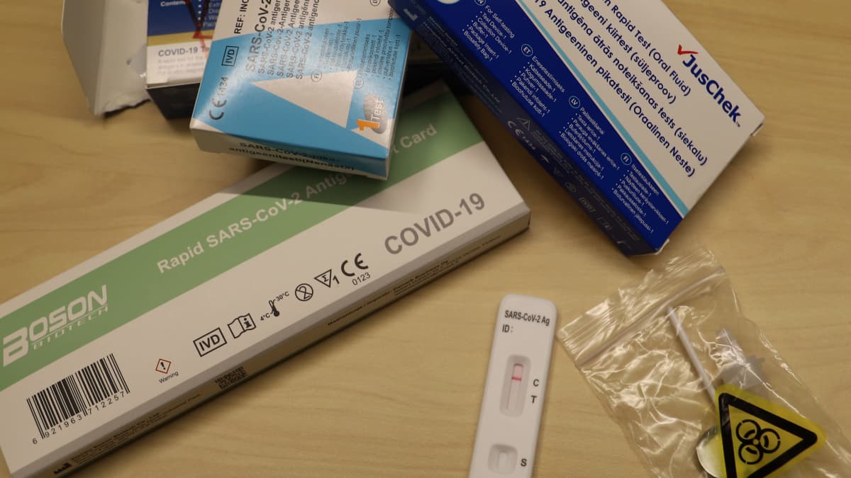 Fyra olikfärgade förpackningar med självtest för covid-19, ett använt negativt test, och en liten plastpåse för kontaminerat avfall