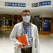 Medelålders man i munskydd och läkarrock. I bakgrunden en sjukhusaula.