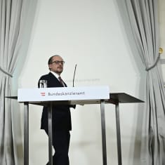 Mies kävelee puhujapaikalle, taustalla Itävallan ja EU:n liput