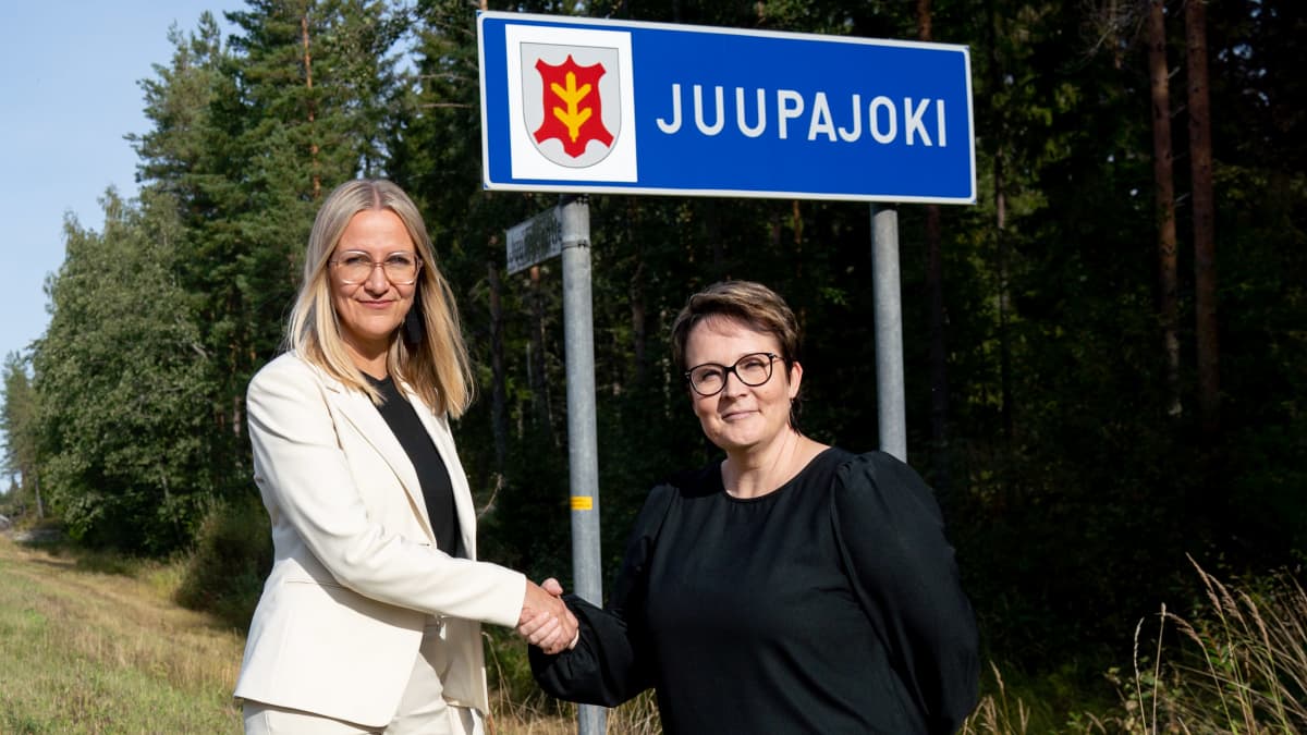 Oriveden kasvatus- ja opetusjohtaja Mia Mattila (vasemmalla) ja Juupajoen hyvinvointijohtaja Anne Tuovila kättelevät Juupajoen rajakyltin alla.
