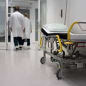 Lääkärit kävelevät Keski-Suomen keskussairaala Novan päivystyksen käytävällä. Käytävän seinustalla seisoo tyhjä potilassänky. 