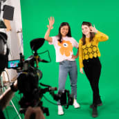 Kaksi naista heiluttamassa kameralle studiossa vihreän taustan edessä.