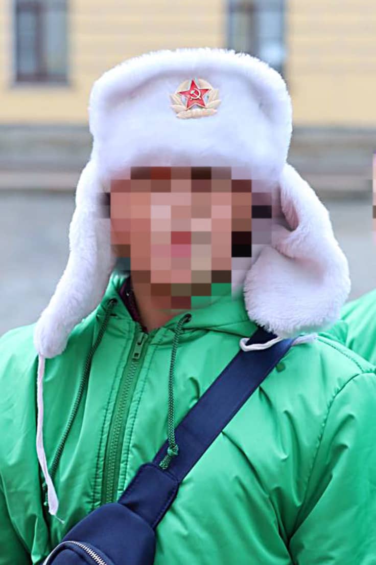 Kaksi henkilöä joiden kasvot on pikselöity tunnistamisen estämiseksi. Keskellä olevalla henkilöllä on päässään valkoinen karvahattu jossa on puna-armeijan symboli, vasara ja sirppi punatähden sisällä.