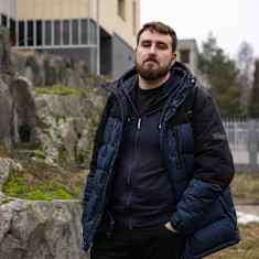 Mies seisoo kivien edessä ulkona pukeutuneena siniseen toppatakkiin.