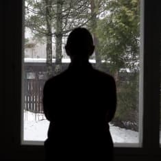 Photo shows the silhouette of a person standing in front of a window.