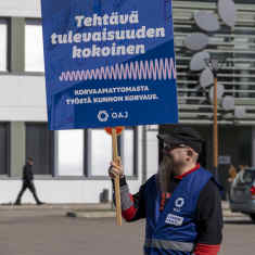 logistiikka-alan opettaja Tommi Miettinen seisoo ammattikoulun edessä lakkovahtina ja pitelee sinistä kylttiä.