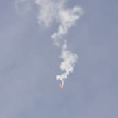 En nödraket dalar röd ner från blå himlen, med ett vitt rökmoln efter sig.