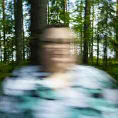 Vaaleaan paitaan pukeutunut nainen seisoo metsässä. Kuvan liike-epäterävyys estää naisen tunnistamisen.