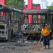 Nainen lakaisee katua kahden tuhoutuneen bussin edessä Sri lankan pääkaupungissa Colombossa