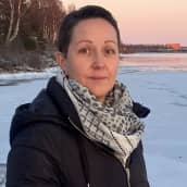 Jonna Pakisjärvi katsoo kameraan osin jäätyneen Kemijoen rannalla punertavan auringonlaskun aikaan..