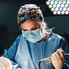 En kirurg håller i ett verktyg och tittar ner på en kropp.