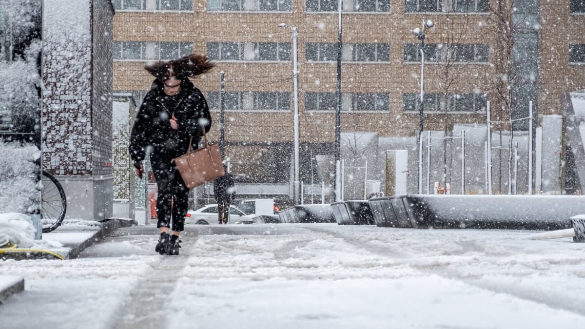 Henkilö kävelee lumisateessa Helsingissä.