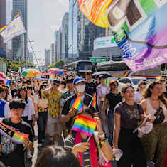 Prideparad i Seoul. En stor skara människor går tillsammans och viftar med regnbågsflaggor.