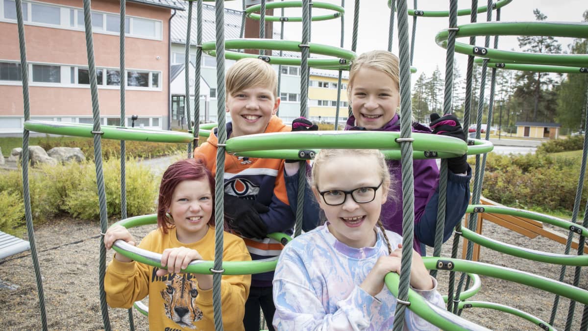 Hymyileviä lapsia kiipeilytelineessä koulun pihalla.