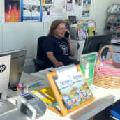Kaksi naista tietokoneiden takana matkailuneuvonnassa. Toinen katsoo kameraan ja hymyilee, toinen puhuu puhelimessa.