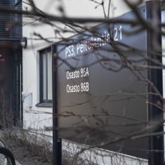 Musta osastokyltti, polkupyoriä telineessä rakennuksen edustalla. 
