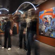 Taidenäyttely Kuopion taidemuseossa. Muoti-aiheisessa näyttelyssä ihmisiä heiluttaa valotikkuja maalauksien edessä.