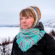 Kvinna står i samisk huvudbonad med Tana älv och fjäll i bakgrunden.