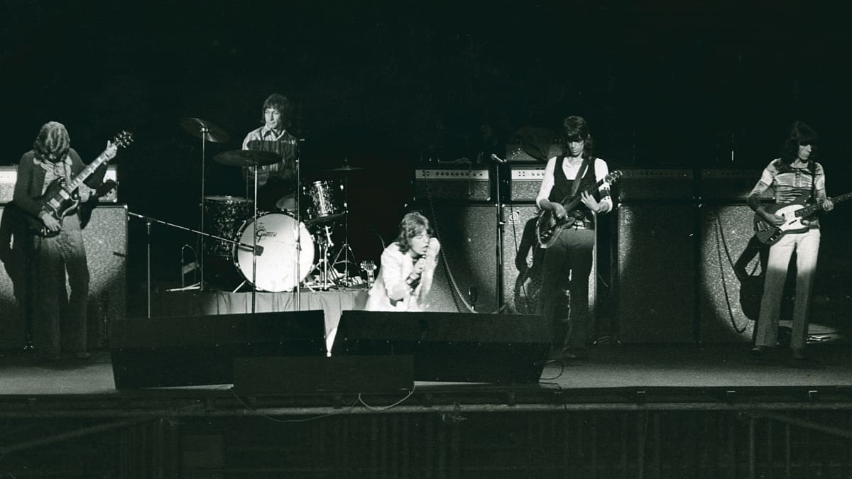 Rock-yhtye Rolling stones esiitymässä. Miehet rivissä lavalla valoheitinten loisteessa. 