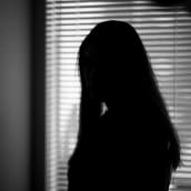 En svartvit bild på kvinna med långt hår vid ett fönster med spjälgardiner.