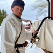 En man klädd i kläder från vinterkriget står bredvid en häst och håller i seldonen.