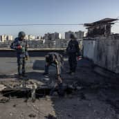 Suojavarusteisiin pukeutuneet henkilöt auttavat asukasta ulos talon katossa olevasta reiästä.