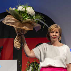 Anna-Maja Henriksson håller i en bukett med blommor och ler. Hon står på en scen klädd i vit skjorta och rosa kjol.