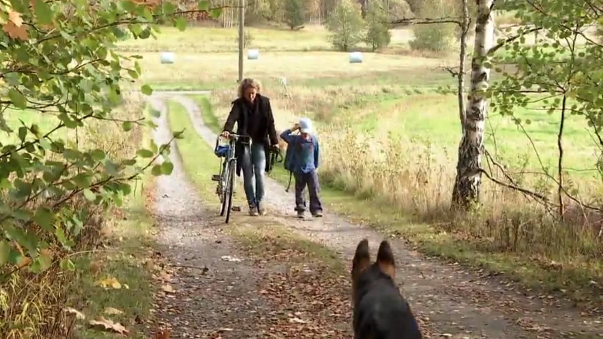 En mamma med sitt barn kommer gående, mamma leder en cykel.