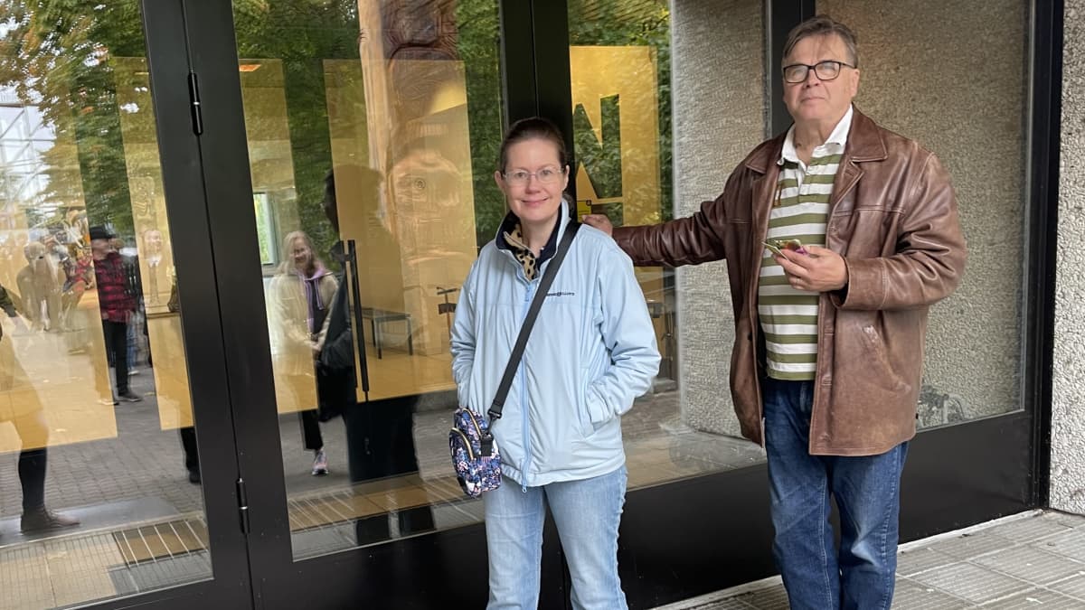Heidi ja Jyrki Kilpikari seisovat taidemuseon ovella ja hymyilevät kameralle. Jyrki pitää kiinni oven kahvasta.