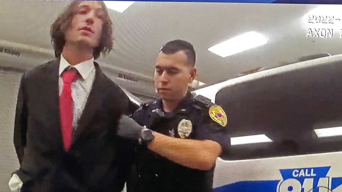 Ezra Miller poliisin otteessa kädet selän taakse kahlittuna.