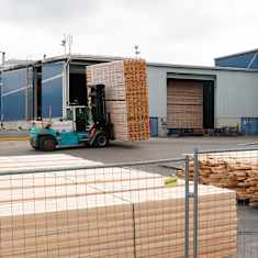 Trukit kuljettavat lautapinoja sahan pihalla.