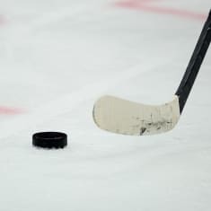 Jääkiekkomaila ja kiekko jäässä yleiskuvassa.