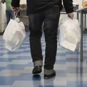 Mies kantaa kahta muovikassia Jyväskylän ruoka-avussa. Kassit ovat täynnä avustusruokaa. 