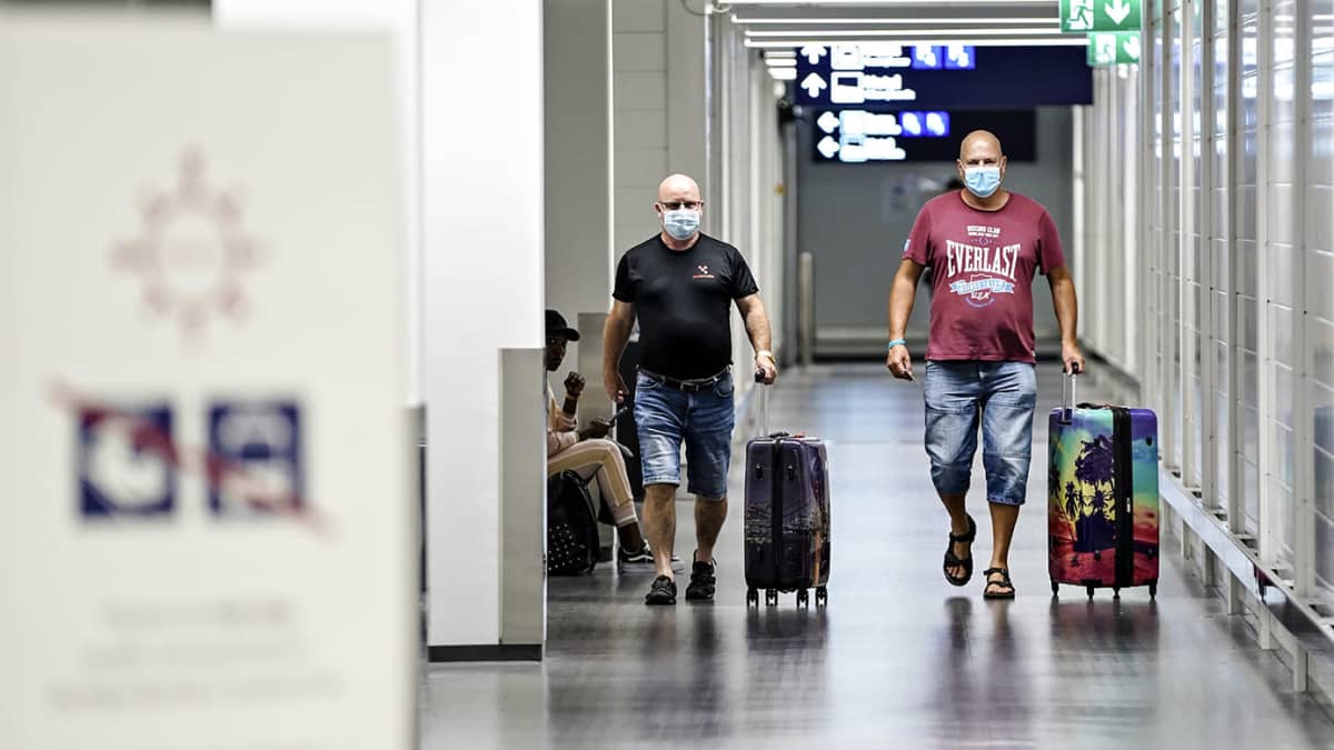 Kaksi matkustajaa kävelee matkatavaroidensa kanssa Helsinki-Vantaan lentoasemalla 7. elokuuta 2020. Kasvojensa edessä heillä on kasvomaskit.