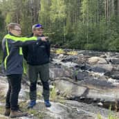 Mikael Rytkönen osoittaa koskelle päin ja Jaakko Muurimäki katsoo osoitettuun suuntaan, taustalla Sapsokoski. 