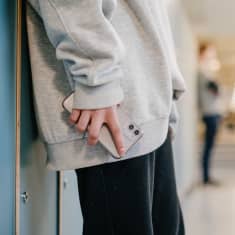 Tunnistamaton oppilas seisoo koulun käytävällä puhelin kädessä.