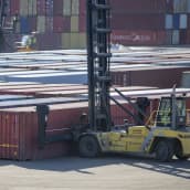 satamakentällä satoja kontteja riveissä ja pinoissa. Etualalla satamatrukki nostaa konttia ilmaan