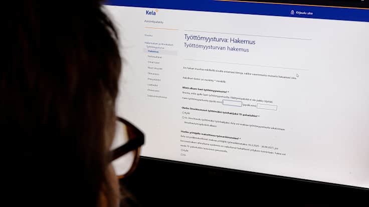 Henkilö tietokoneen näytön äärellä, jossa Kelan on työttömyysturvahakemus.