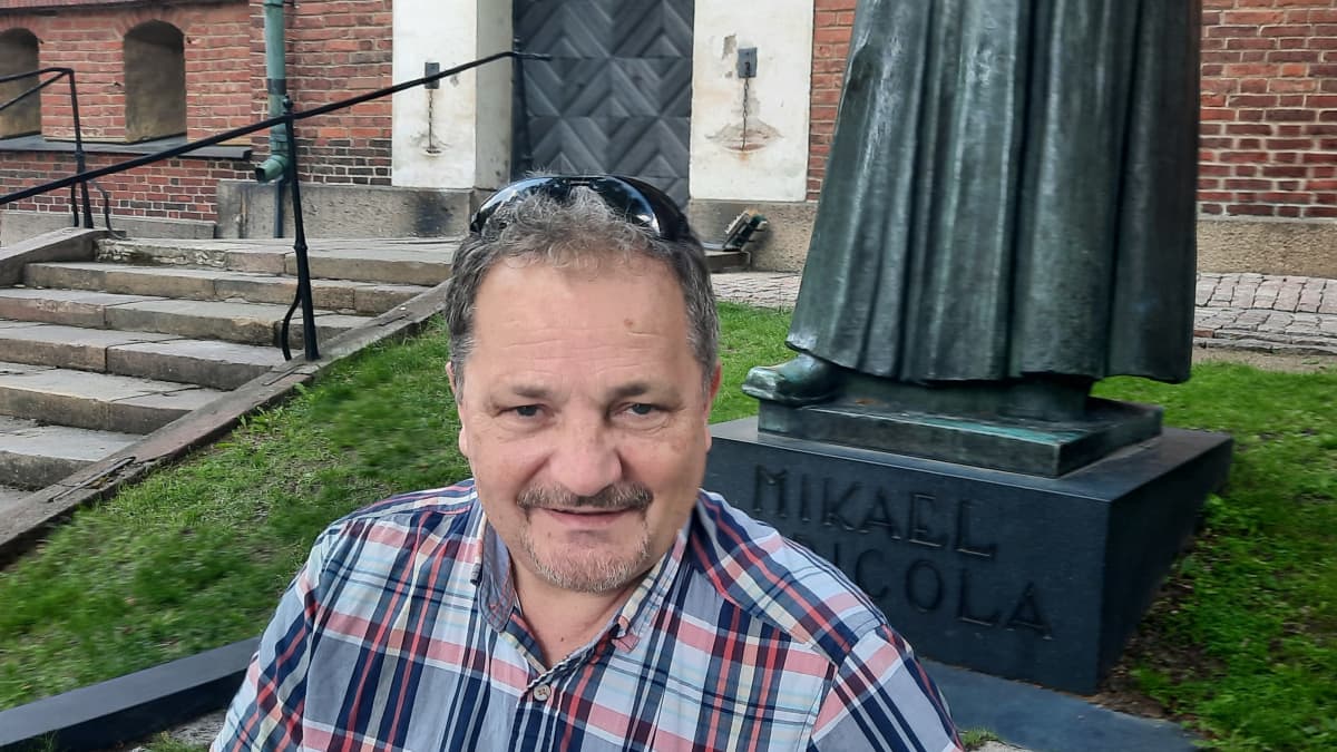 Kirjailija elokuvaohjaaja Janne kuusi istuu Turun Tuomikirkon edessä Mikael Agricolan patsaan juurella 