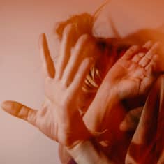 Naishenkilö pitää käsiä kasvojen edessä.