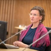 Miina Seurujärvi istuu kokoushuonessa edessään mikrofoni ja läppäri.  
