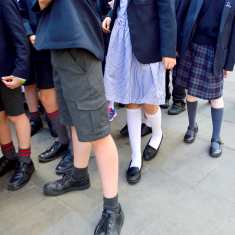 Englantilaisiin koulu-univormuihin pukeutuneiden lasten jalkoja.