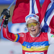 Therese Johaug tuulettaa Norjan lippu molemmissa käsissään.