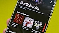 A closeup photo of a hand holding a smartphone showing Spotify's audiobook page.