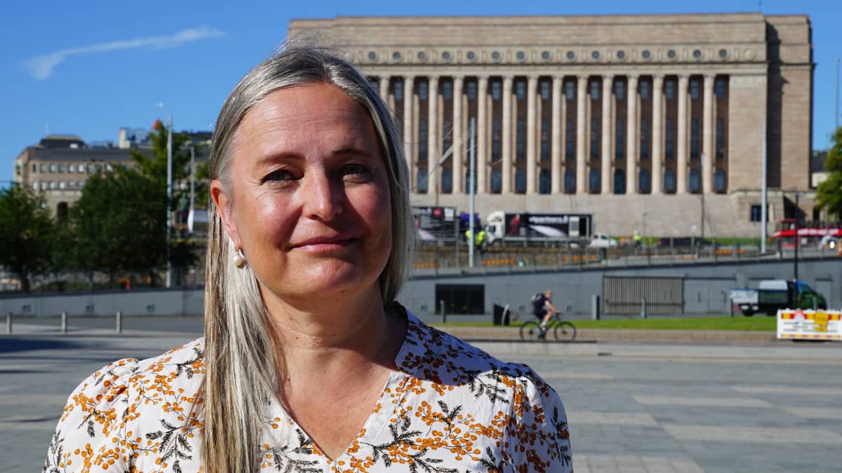 Iro Särkkä, vanhempi tutkija, Ulkopoliittinen  instituutti Eduskunta takanaan katsoo kameraan.