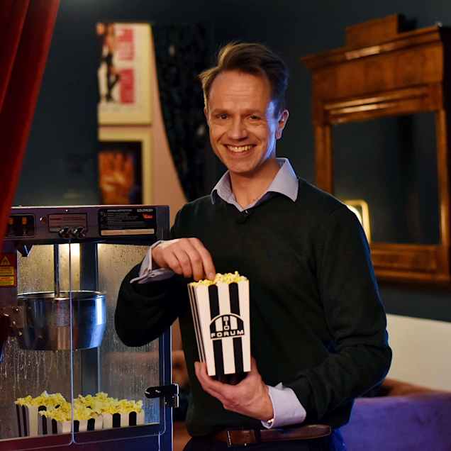 En man äter popcorn och ser in i kameran och ler. 