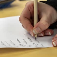 Kuudesluokkalainen tyttö kirjoittamassa allekirjoitusta lyijykynällä. Vieressä näkyy luokkakavereiden tekemiä allekirjoituksia.