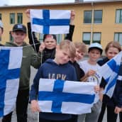 Kahdeksan ala-asteikäistä poikaa seisoo Sääksjärven koulun pihalla pidellen Suomen lippuja. Taustalla näkyy koulurakennus.