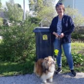 Meri-Lapin koiraklubin puheenjohtaja Maija Saarenpää koiransa Tuuman kanssa seisoo omakotitalon jäteastian vieressä.